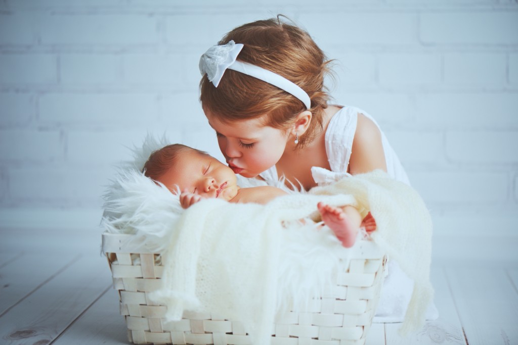 children sister kisses brother  newborn sleepy  baby on a light background