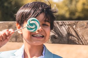 Leuke communiefoto van jongen met lolly voor zijn gezicht