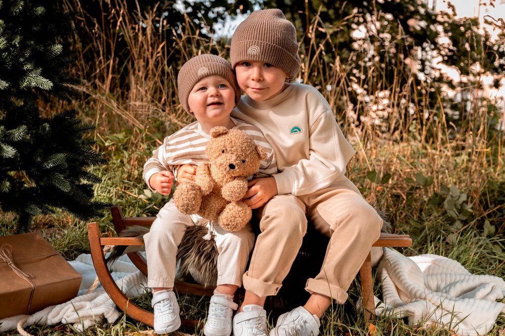 2 broertjes poseren op een slee voor een kerstfoto met een teddybeer
