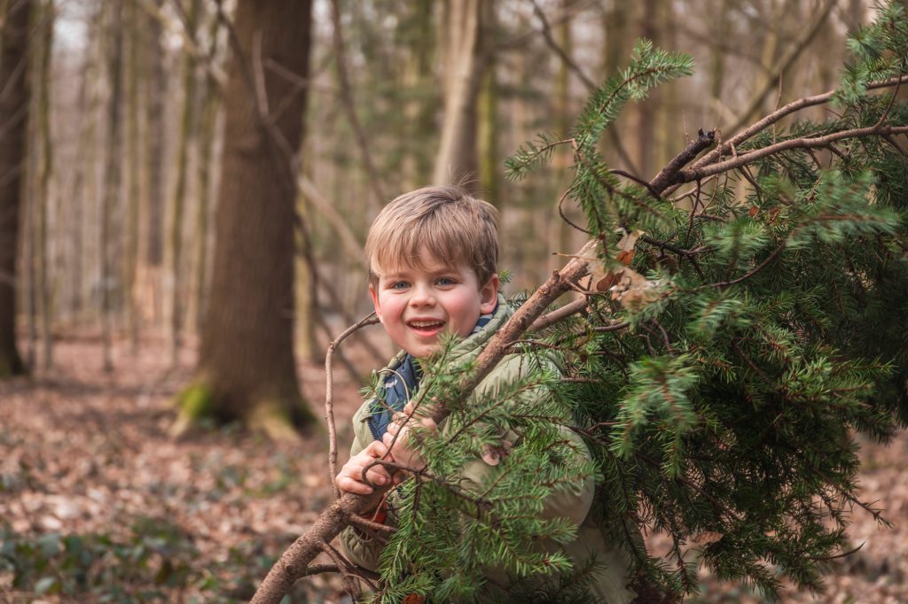 jongen poseert voor kerstfoto en loopt rond in bos met een dennentak
