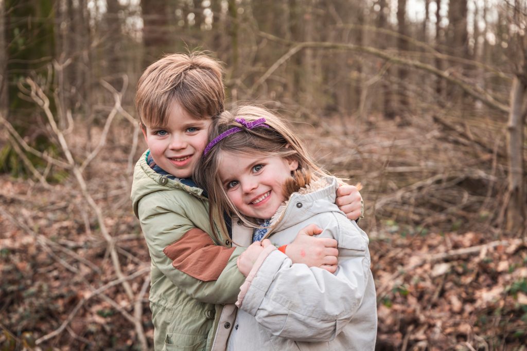 broertje en zusje knuffelen in bos en poseren voor een kerstfoto