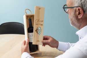 Man opent een houten wijnkist met een fles rode wijn. De houten wijnkist is gepersonaliseerd met een kerstwens